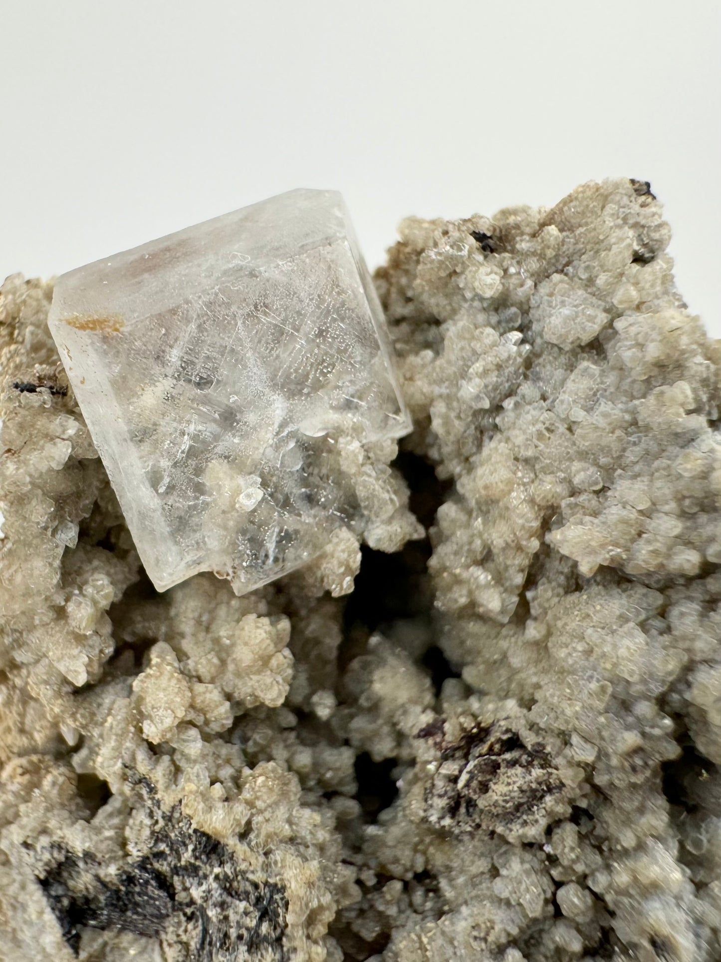 Detail of the hydroxyapophyllite crystal with good translucency, the calcite druzy is visible through it and included inside it. The crystal has a light crosshatch pattern.