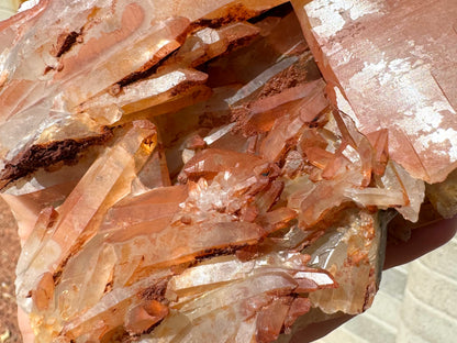 Detail of different sizes of quartz crystals in the cluster of the base, some fairly colorless and others tinted yellow to red with hematite. There is some sandy opaque red mineral on areas.