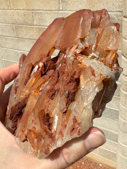 A side view of the piece, less saturated orange-red on the lower right side. There are clusters of opaque red minerals among the small points at the base of the piece.