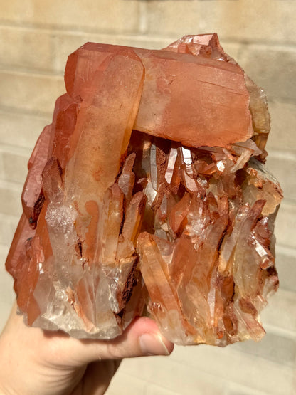 A large red quartz specimen, a cluster of dozens of points of multiple sizes with on large tabular crystal perched horizontally across the top of the piece.