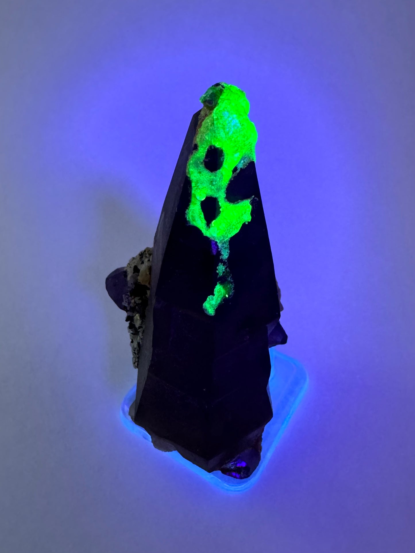 The second of three lighting images: the piece in the same position as the previous image, in low lighting illuminated with blue-tinted UV light. The hyalite fluoresces strong yellowish-green with a slight icy-blue overtone.