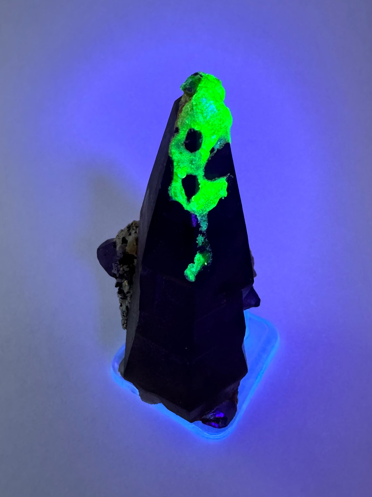The second of three lighting images: the piece in the same position as the previous image, in low lighting illuminated with blue-tinted UV light. The hyalite fluoresces strong yellowish-green with a slight icy-blue overtone.