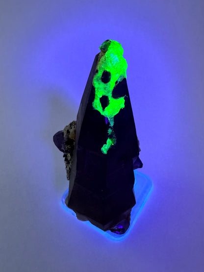 The second of three lighting images: the piece in the same position as the previous image, in low lighting illuminated with blue-tinted UV light. The hyalite fluoresces strong yellowish-green with a slight icy-blue overtone.