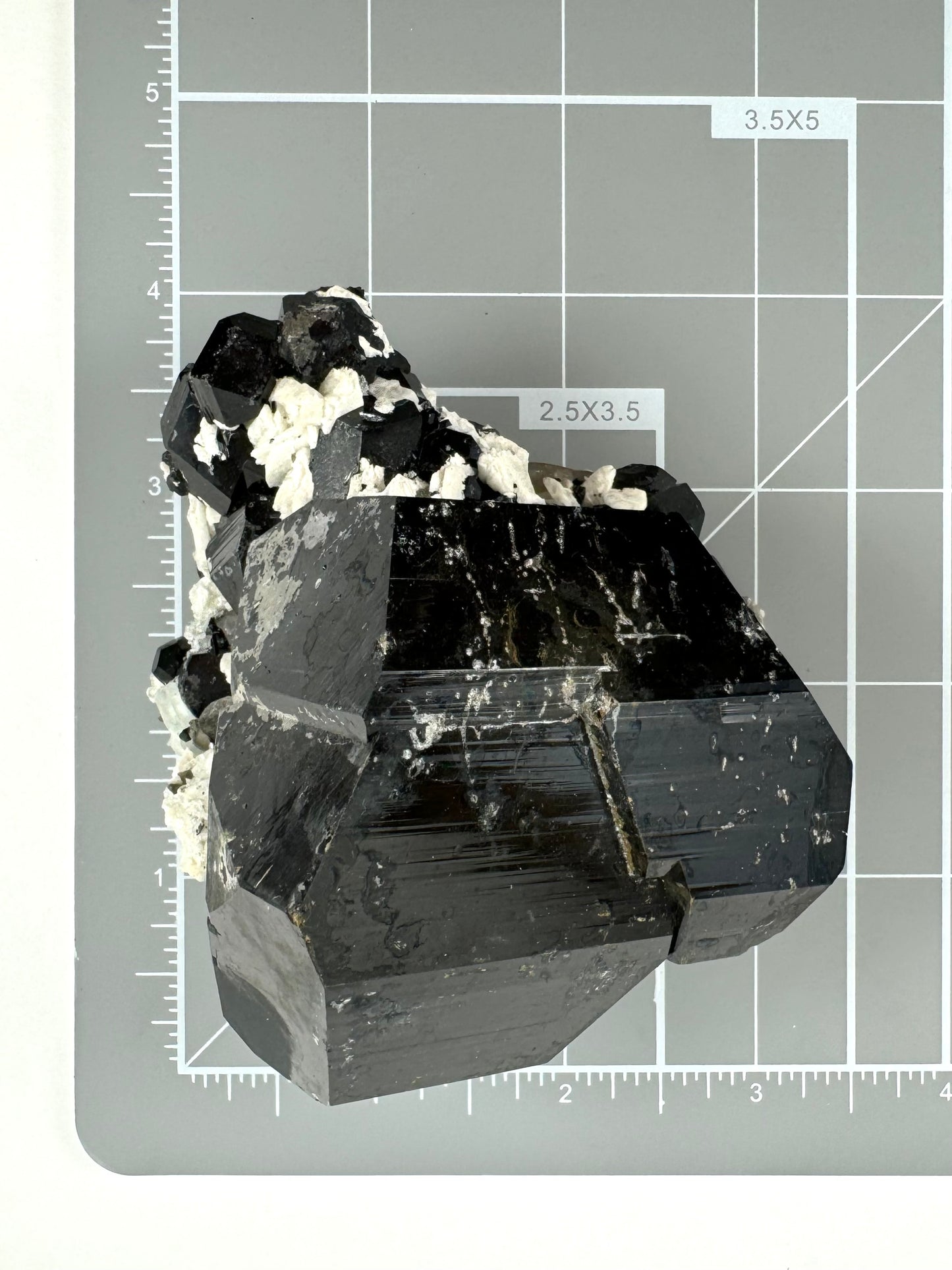 Scale image of the specimen on a measuring mat, measuring about three inches square with a cluster of crystals on one end adding close to an inch.