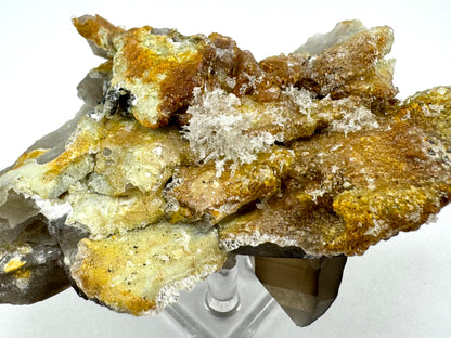 Detail of the underside of the specimen with a cluster of whitish needles in the center of a large area covered in hyalite. The underside has layers of shard-like smoky quartz, with a golden yellow mineral under the hyalite.