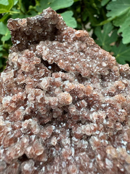 Detail view of the calcite druzy, showing colorless crystals with fine brick-red spots in the core. The druzy has triangular and rhombohedral crystal faces.