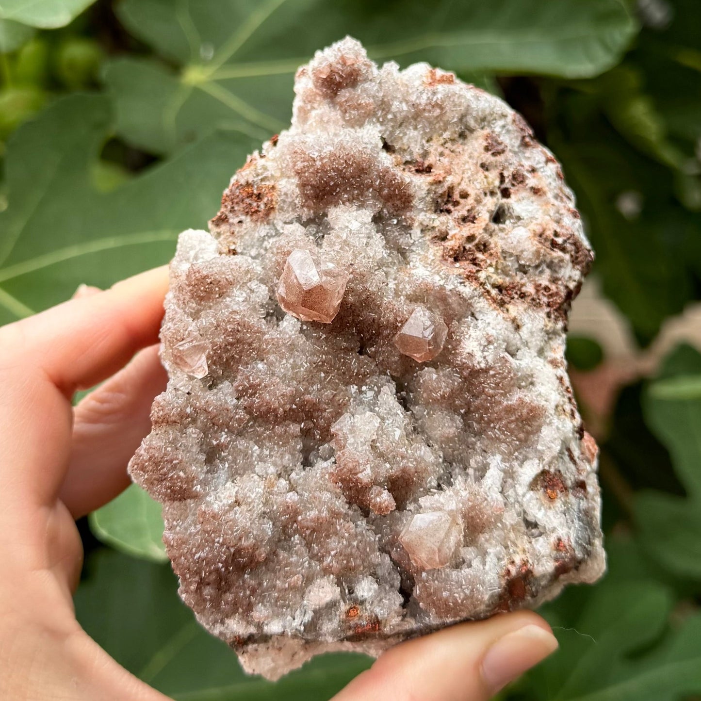 The front of an irregular-shaped calcite specimen with druzy and large crystals on a white and red-brown matrix, and dusted with red-brown coloration.