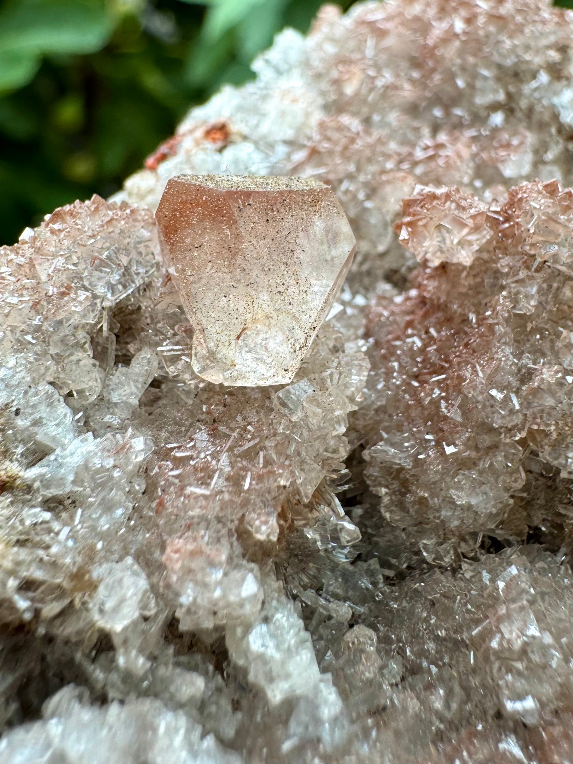 Detail view of a calcite crystal with good trigonal form, colorless with a dusting of red inclusions inside and more brown tinted on the surface. The druzy appears composed of intersecting pyramid-shaped calcite crystals.