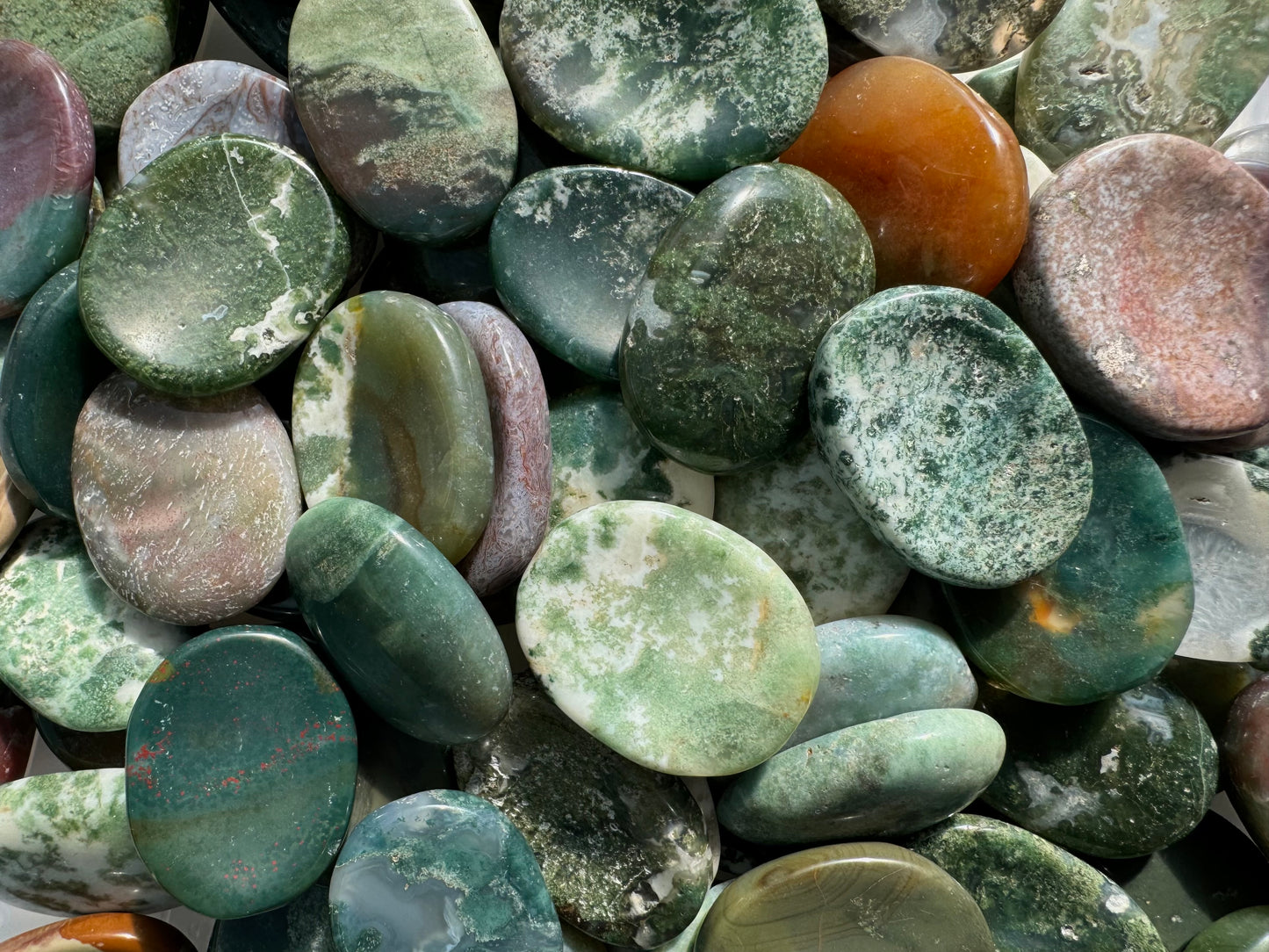 A pile of miscellaneous agate worry stones, primarily green in color with some white and warm tones.