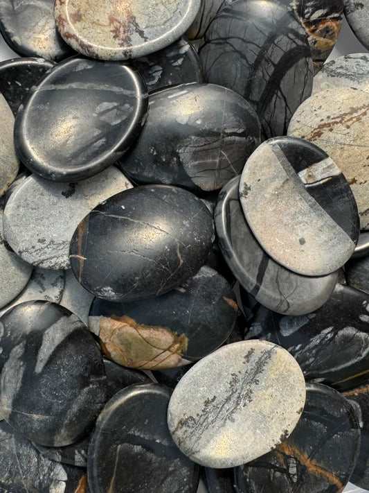 A pile of Picasso jasper worry stones, with angular and veining patterns in tones of gray and black. Some have patterns that look almost dendritic.