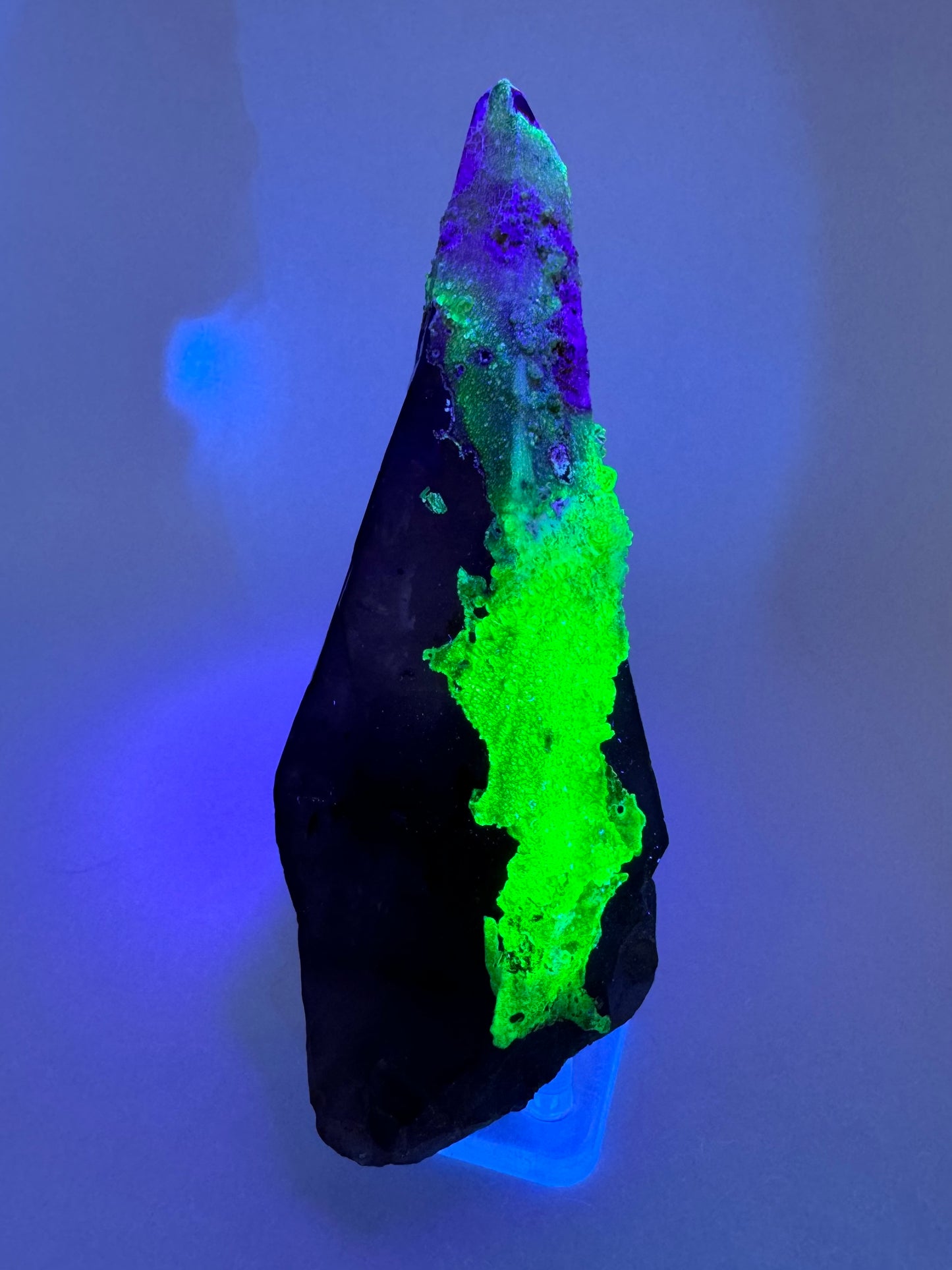 The second of three lighting images: the point in the same position as the previous image, in the dark and illuminated with blue-tinted UV light. The hyalite fluoresces a strong yellowish-green with light blue in the hyalite in the top half.