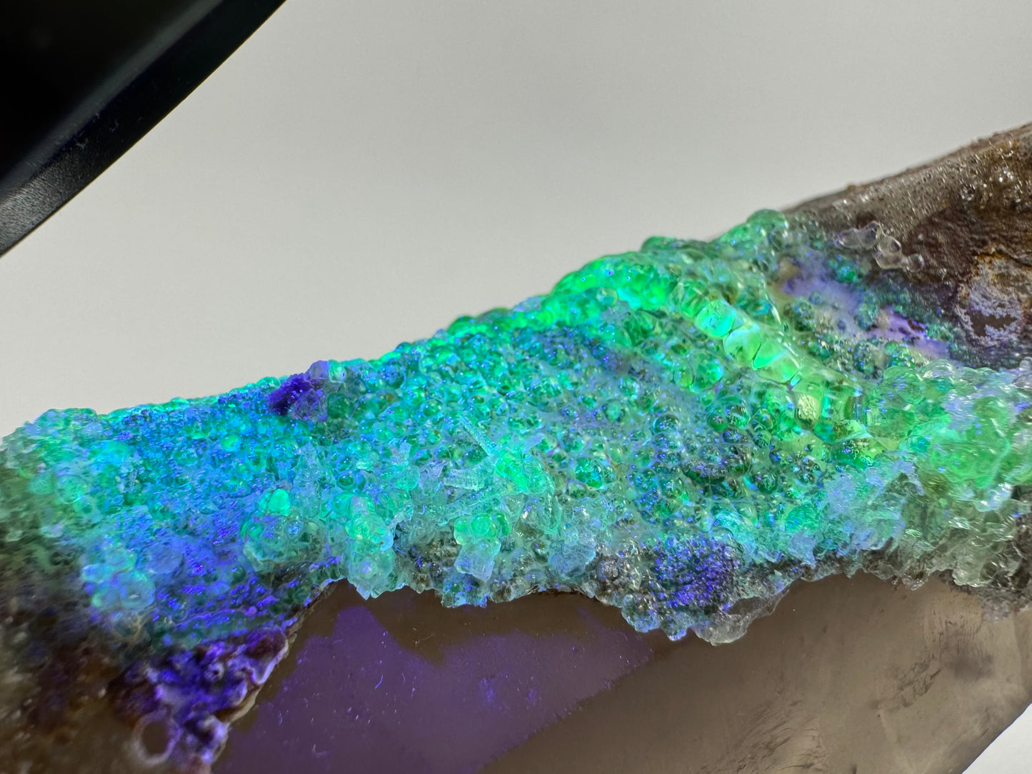 The third of three lighting images: the point in the same position as the previous image,  in lower light and illuminated with UV light. The hyalite fluoresces a moderate yellowish-green with icy-blue.