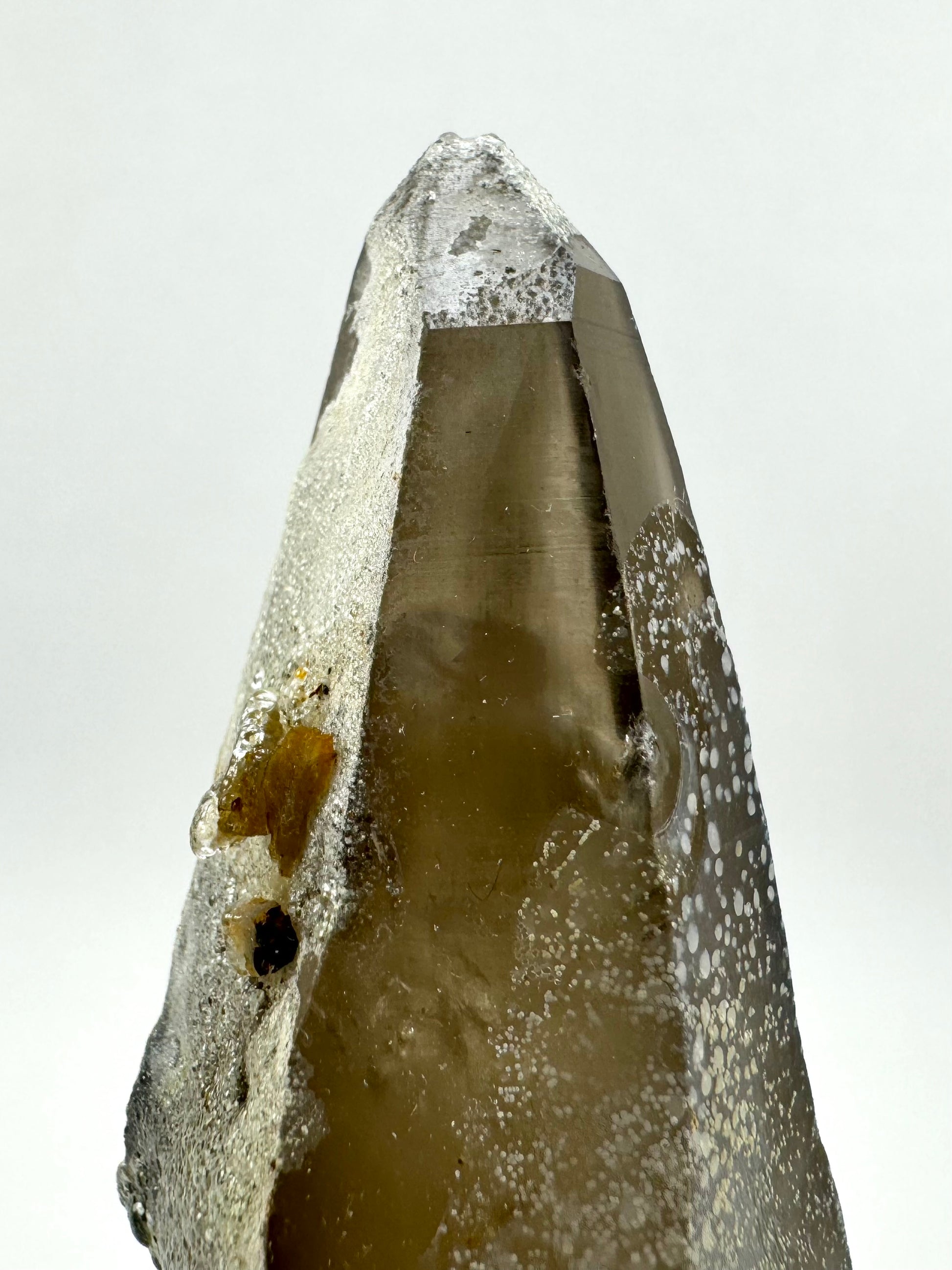 Detail of the tip of the point, with a white overlay covered in hyalite on the left face, and a filmy overlay with white spots on the right face.