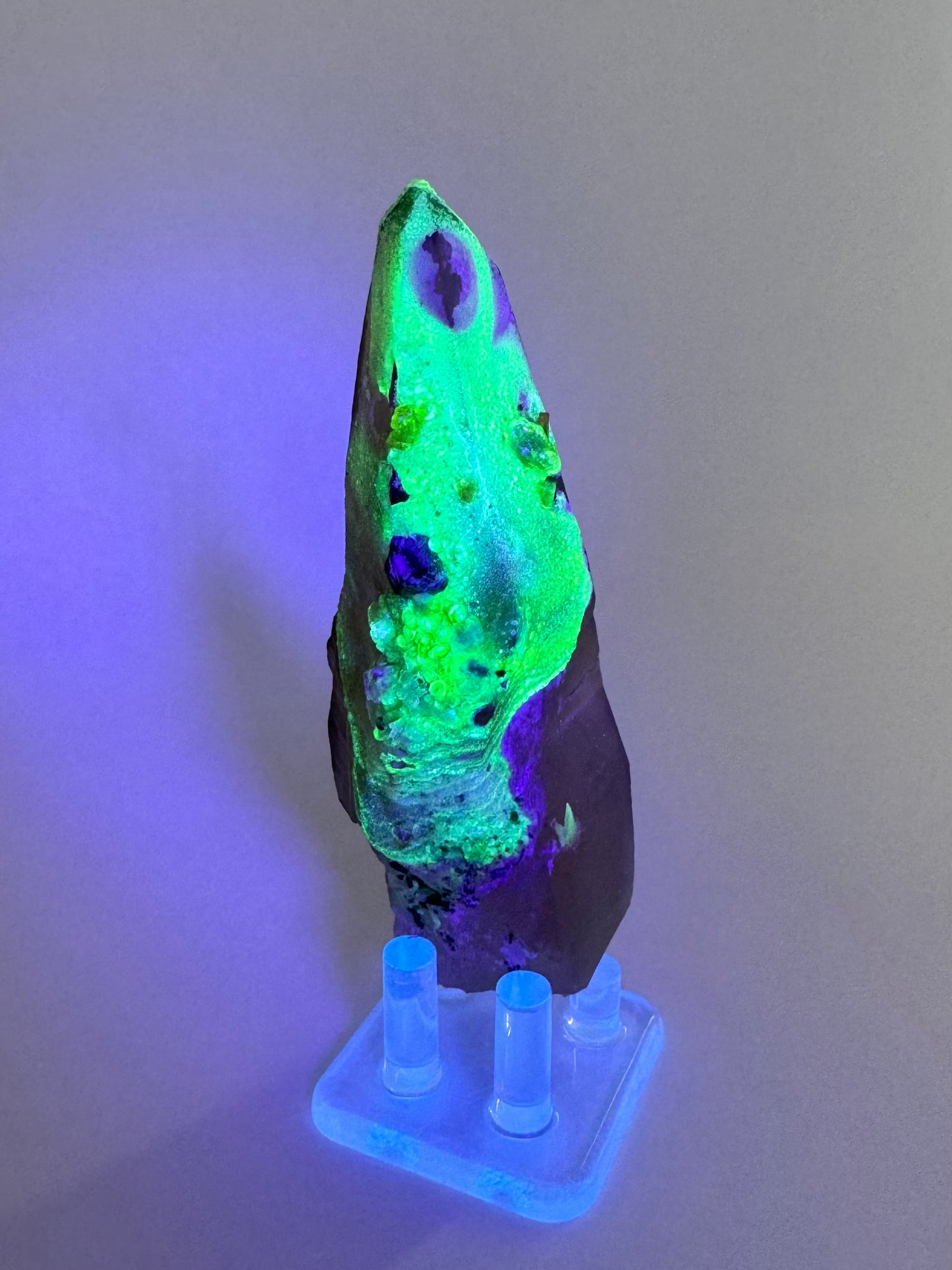 The second of three lighting images: the point in the same position as the previous image in low light, illuminated in blue-tinted UV light. The hyalite fluoresces strong yellowish-green with patches of light blue. The fluorescence is in the shape of a ghost with a tail and  an oval patch missing where its face would be.