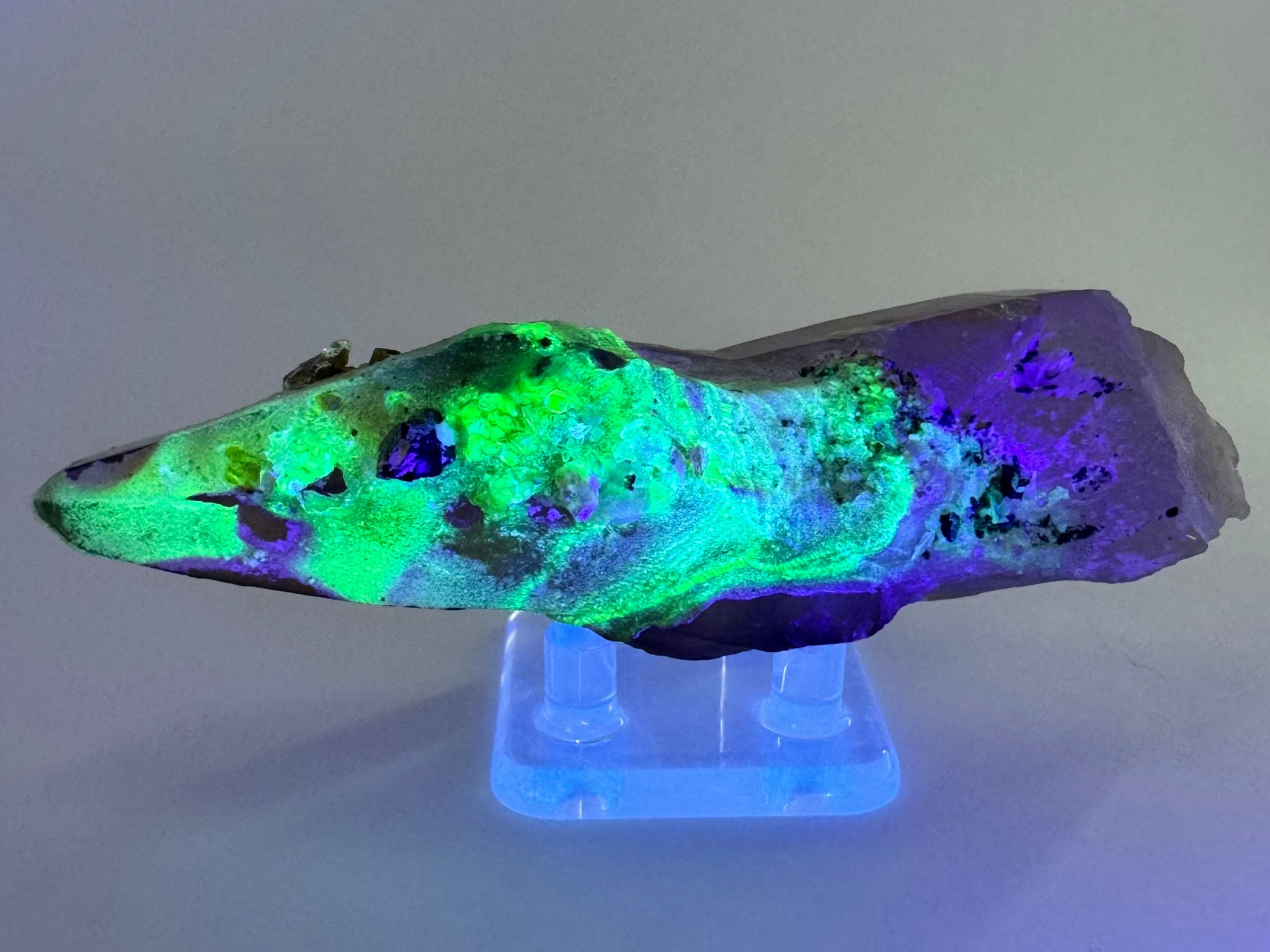 The second of three lighting images: the point in low light in the same position as the previous image, illuminated in blue-tinted UV light. The hyalite fluoresces strong yellowish-green with patches of light blue.