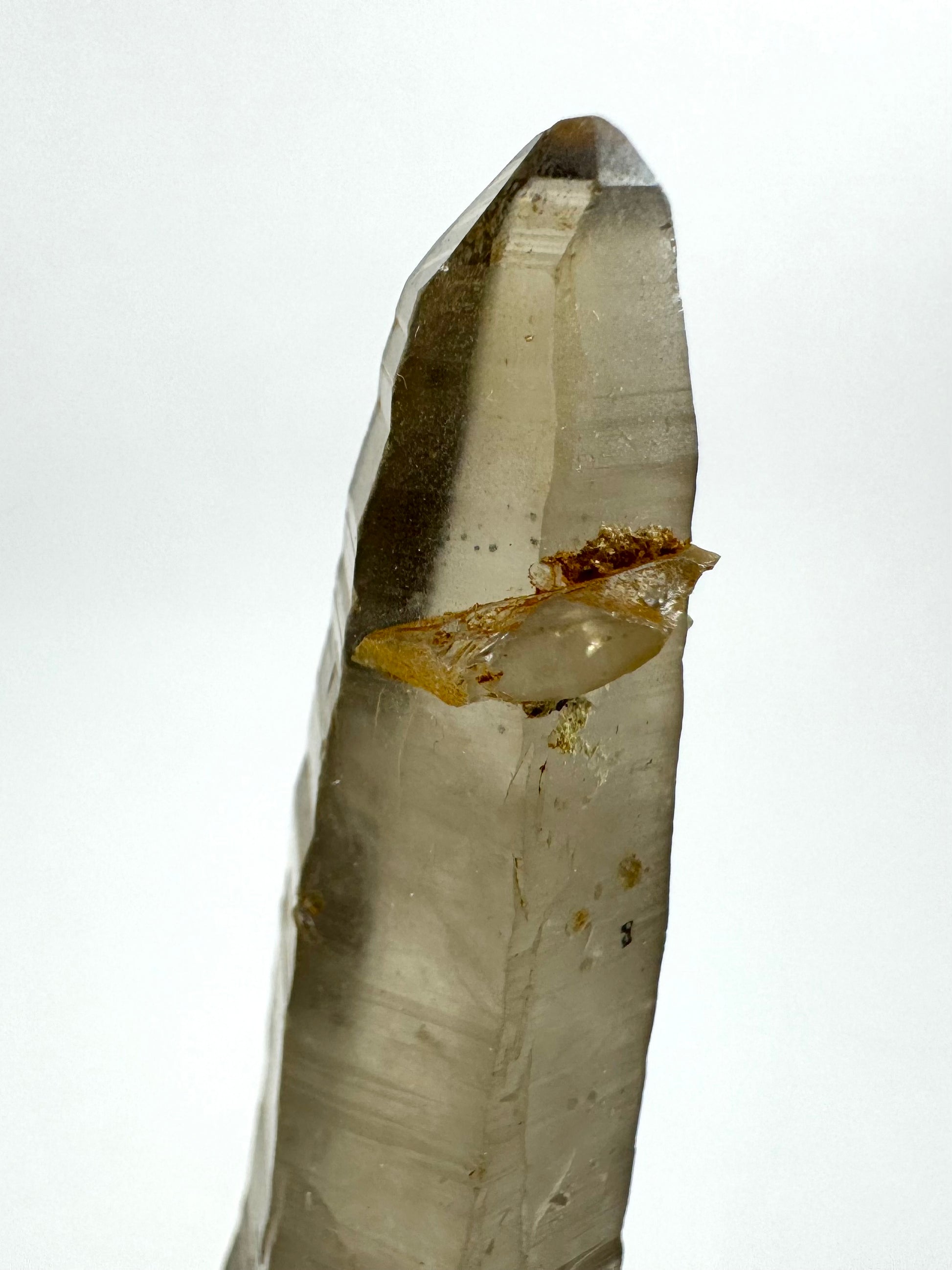 Detail view of the tip of the point which has small faces, and the irregular crystal attached near the tip. It looks like a flat shard of smoky quartz.