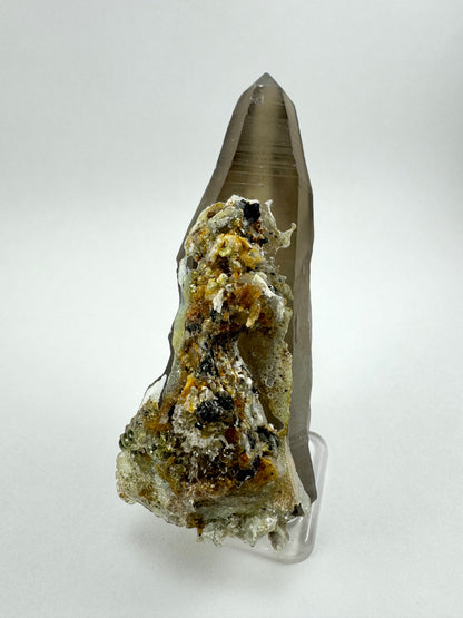 Full view of a well-formed symmetric smoky quartz point, with a large cluster of mixed minerals coated in hyalite covering the bottom two thirds of this side.