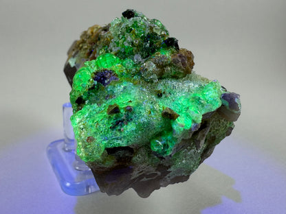 Second of three lighting images: the base of the mineral in dim light illuminated in blue-tinted UV light. The hyalite fluoresces strong slightly blue-tinted yellowish-green.