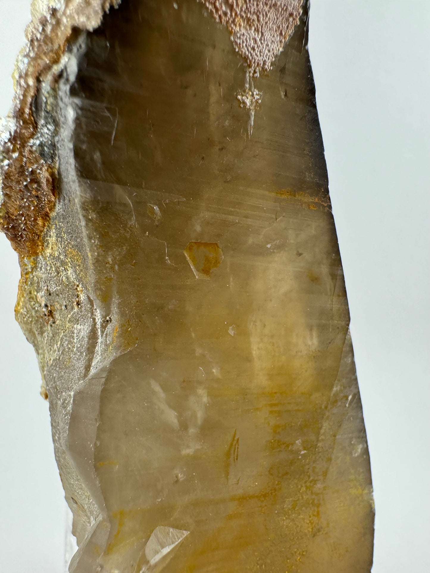 Detail view of a side, showing the translucency of the piece is fairly good and wispy inclusions and feathers are visible inside. The surface has a bit of iron staining, which emphasizes a small hexagonal indentation.