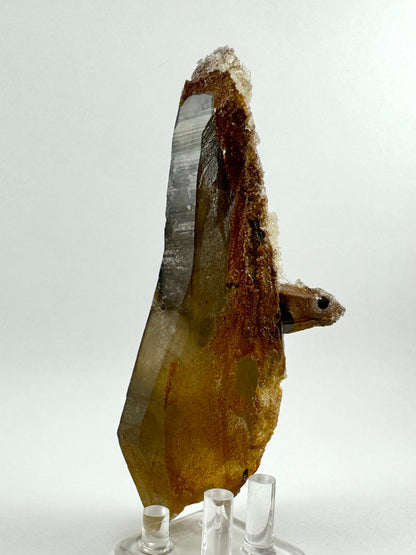 Another side of the specimen, showing the curved back of the point with nice striations on the quartz face. There is red-orange iron staining under the colorless hyalite, which has grown thick enough it's raised off the surface like a crust