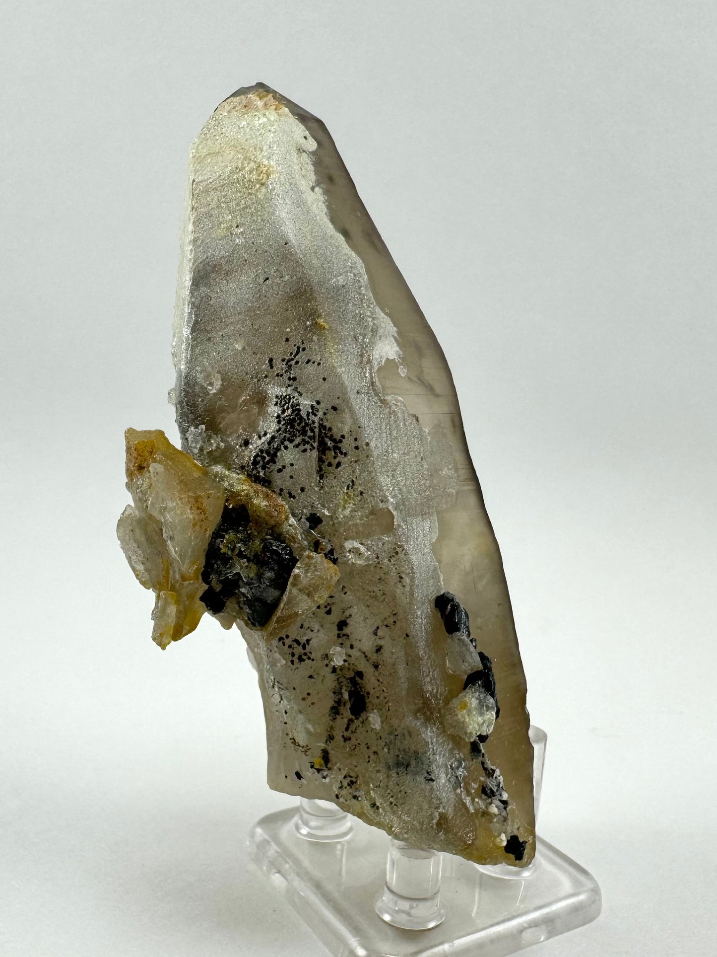 View of the side of the point coated in hyalite, chunks of smoky quartz, and pieces of black schorl. There are also small black spheres sprinkle on the hyalite.