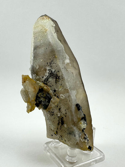 View of the side of the point coated in hyalite, chunks of smoky quartz, and pieces of black schorl. There are also small black spheres sprinkle on the hyalite.