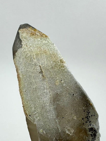 Detail of the tip of the point. A thin layer of off-white hyalite covers it, and has a crackled pattern. In the center, some small pieces of hyalite are missing as if it had been hit there.