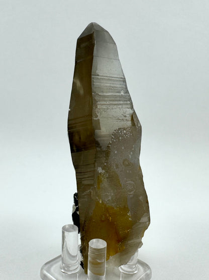 A side of the smoky quartz showing flat, angular faces with good horizontal striations. Milky overgrowth mutes the shine near the base.