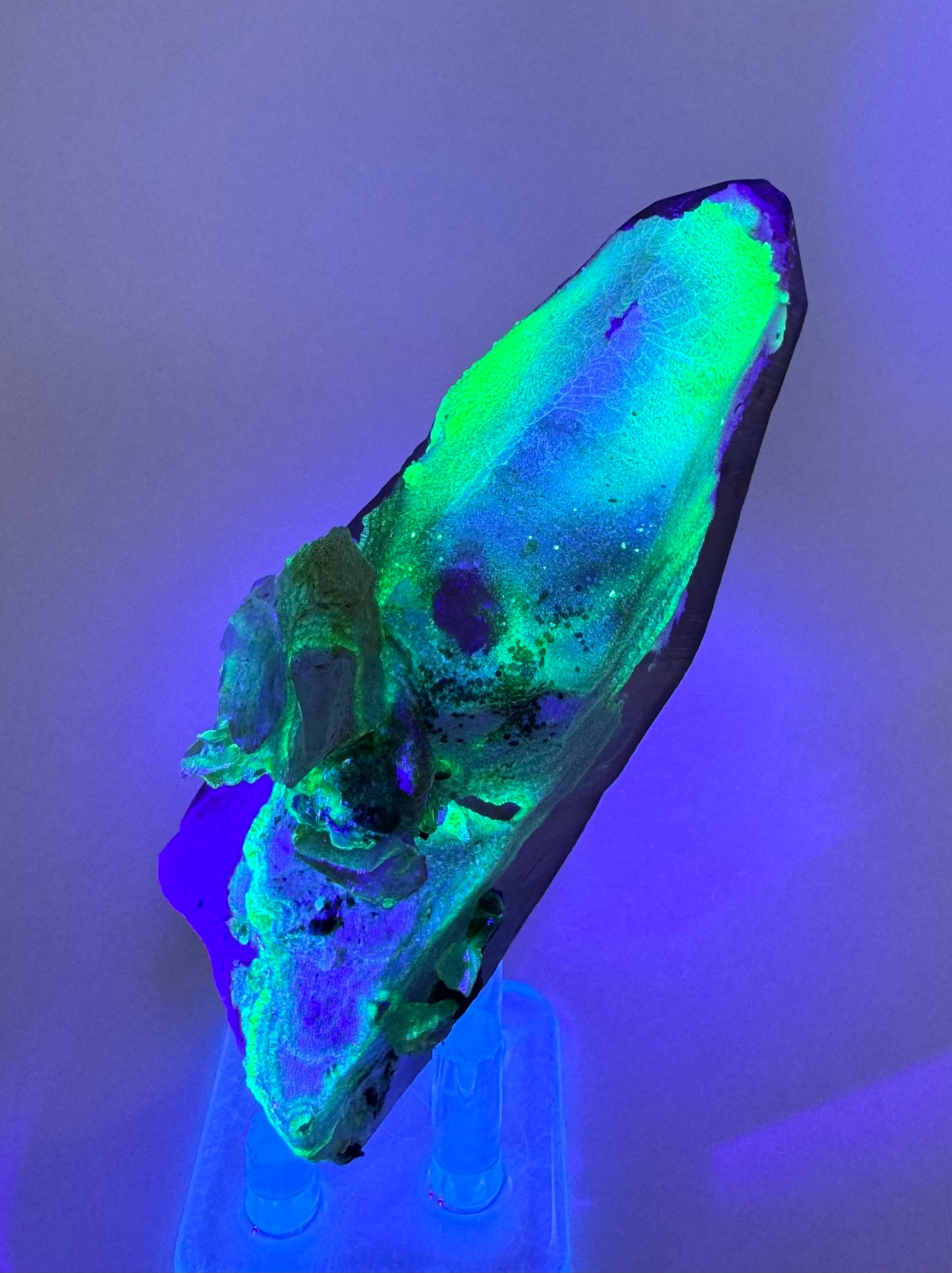 The second of three lighting images: the piece in the same position as the previous image, in low lighting illuminated with blue-tinted UV light. The hyalite fluoresces strong yellowish-green with a light blue color in the center.