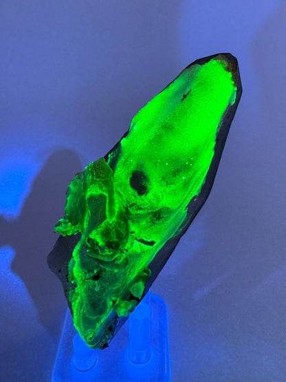 The third of three lighting images: the piece in the same position as the previous image, in low lighting illuminated with blue-tinted UV light. The hyalite fluoresces a strong yellowish-green.