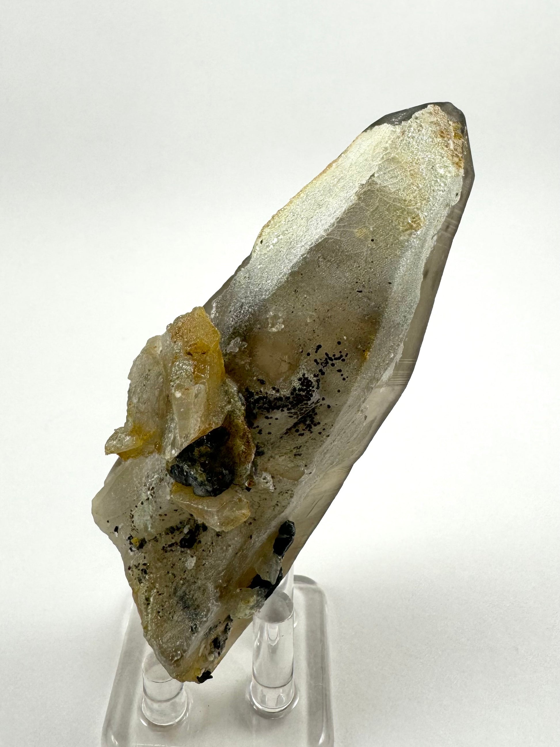 The first of three lighting images: a thick smoky quartz point nearly entirely coated with hyalite on this side, and a cluster of irregular smoky quartz and black crystals near the base.