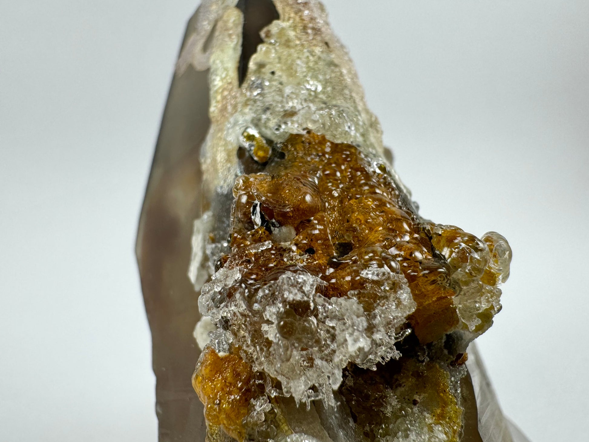 Detail image of glossy hyalite, bubbly botryoidal form of colorless hyalite over orange-brown iron staining, with a cluster of needle-like growth in the foreground.