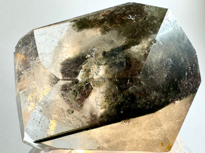 The piece illuminated from below, highlighting the wispy colorless inclusions. There are lumpy light green chlorite inclusions, one of which appears to have been pulled out in polishing leaving an irregular pit on the junction between facets.