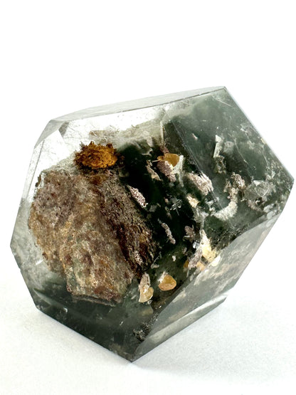 Detail of the bottom of the garden quartz piece in bright white light, showing the hexagonal form on the inclusion through the center surrounded by mossy dark green chlorite and shiny light yellow flake-like inclusions