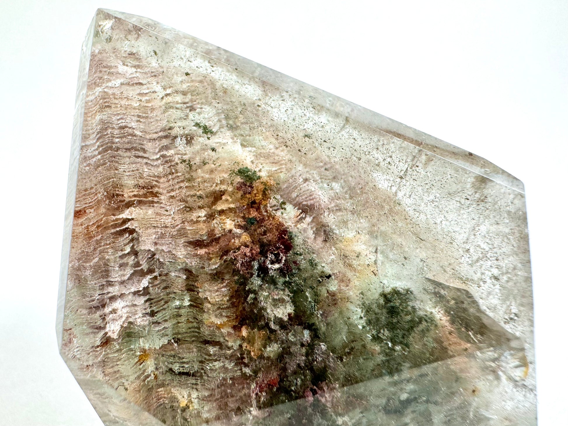 Detail of the tip on the freeform in bright white light, filled with paper-thin layers of light pinkish and off-white chlorite, closely stacked. There are clusters of rust-brown and moss green chlorite.