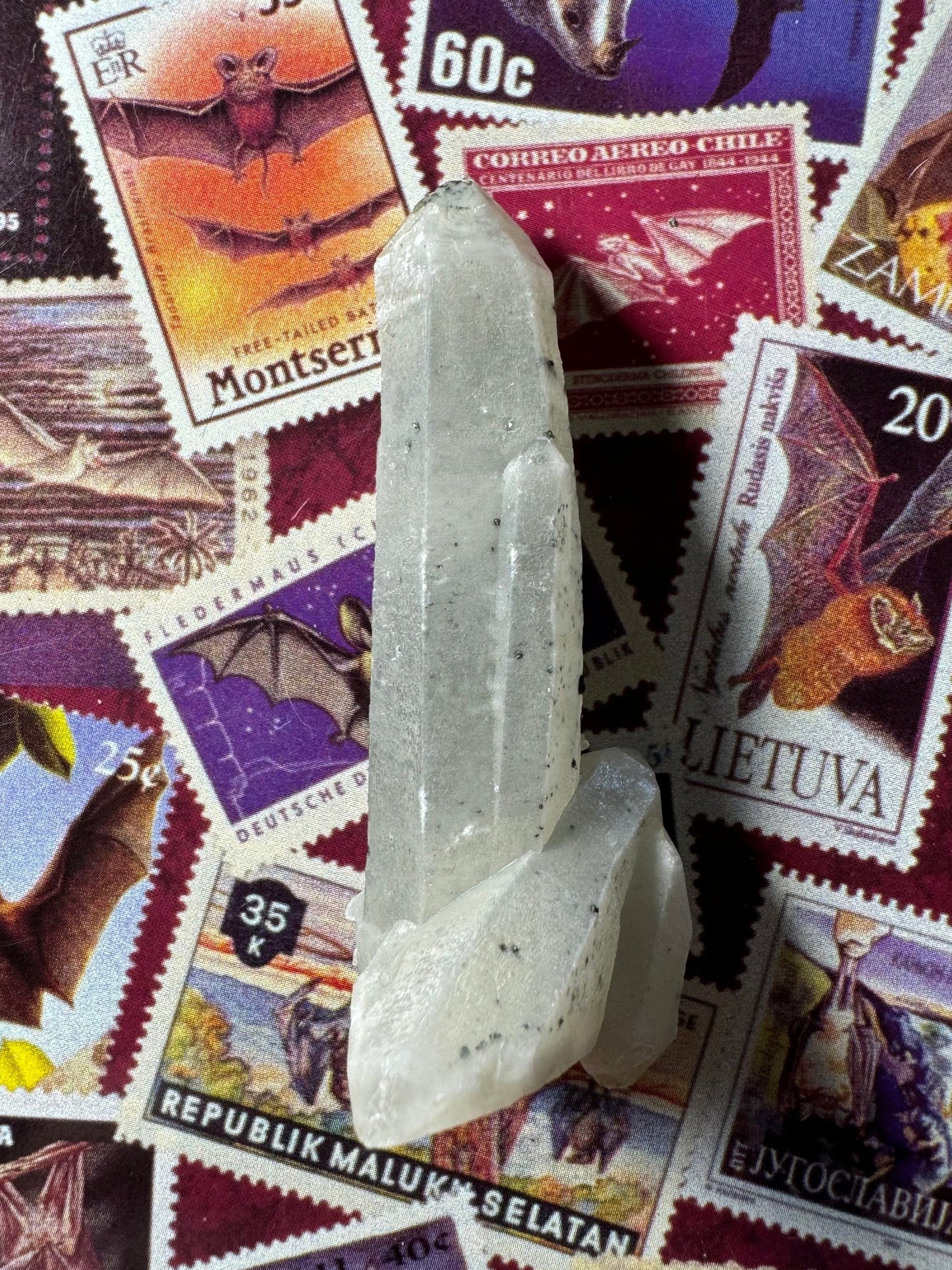 Full view of a translucent white quartz point with additional smaller quartz crystals at the the base. Good quartz crystal forms are highlighted by the opacity. There are small black spot inclusions inside the piece.