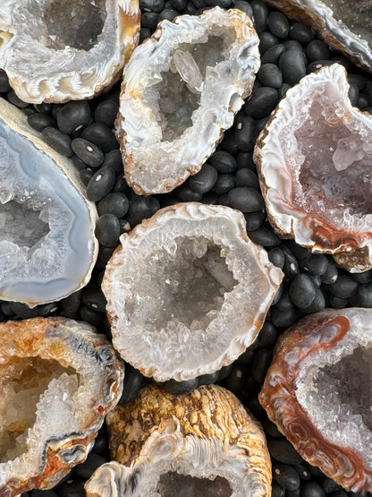 Miscellaneous Oco geodes arranged face-up in dry black beans showing their glittery quartz interiors.