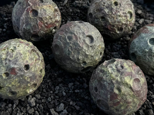 Several small moons carved from dragon's blood jasper spread out on a black lava sand background