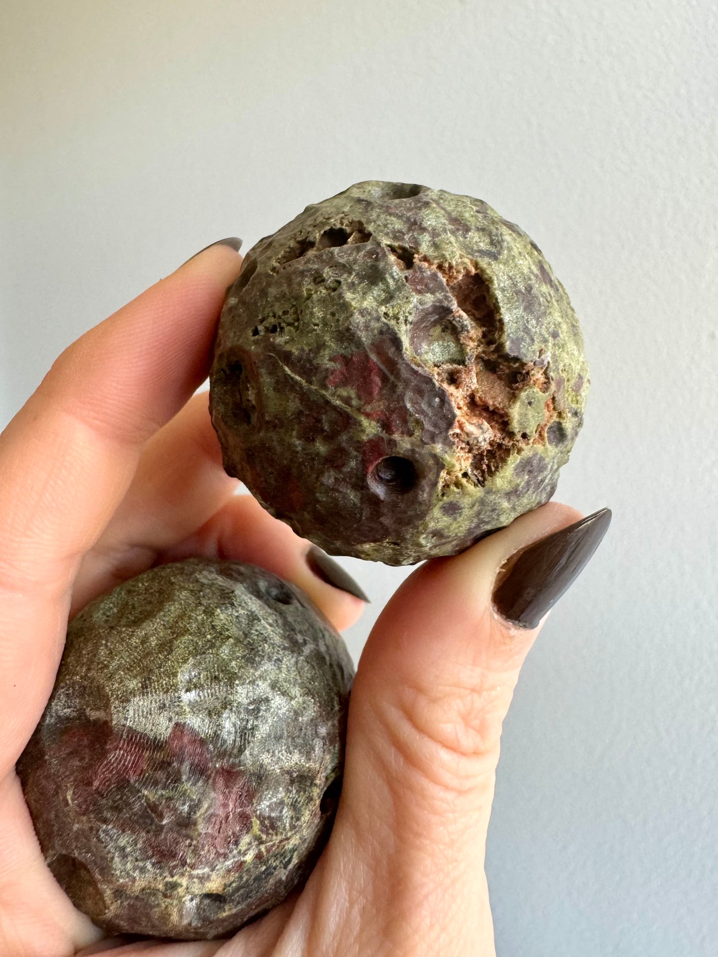 Detail of two of the moons. The top one has a natural cavity in the surface like a valley, tinted a light brown against the green and ed spotting. The bottom has light reflecting off light ridges left by the carving process