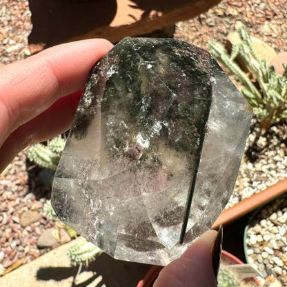 The specimen with sunlight shining directly on it, appearing darker than when side-lit. A lot of the piece is clear with wispy colorless inclusions, and the dark green chlorite at the top.