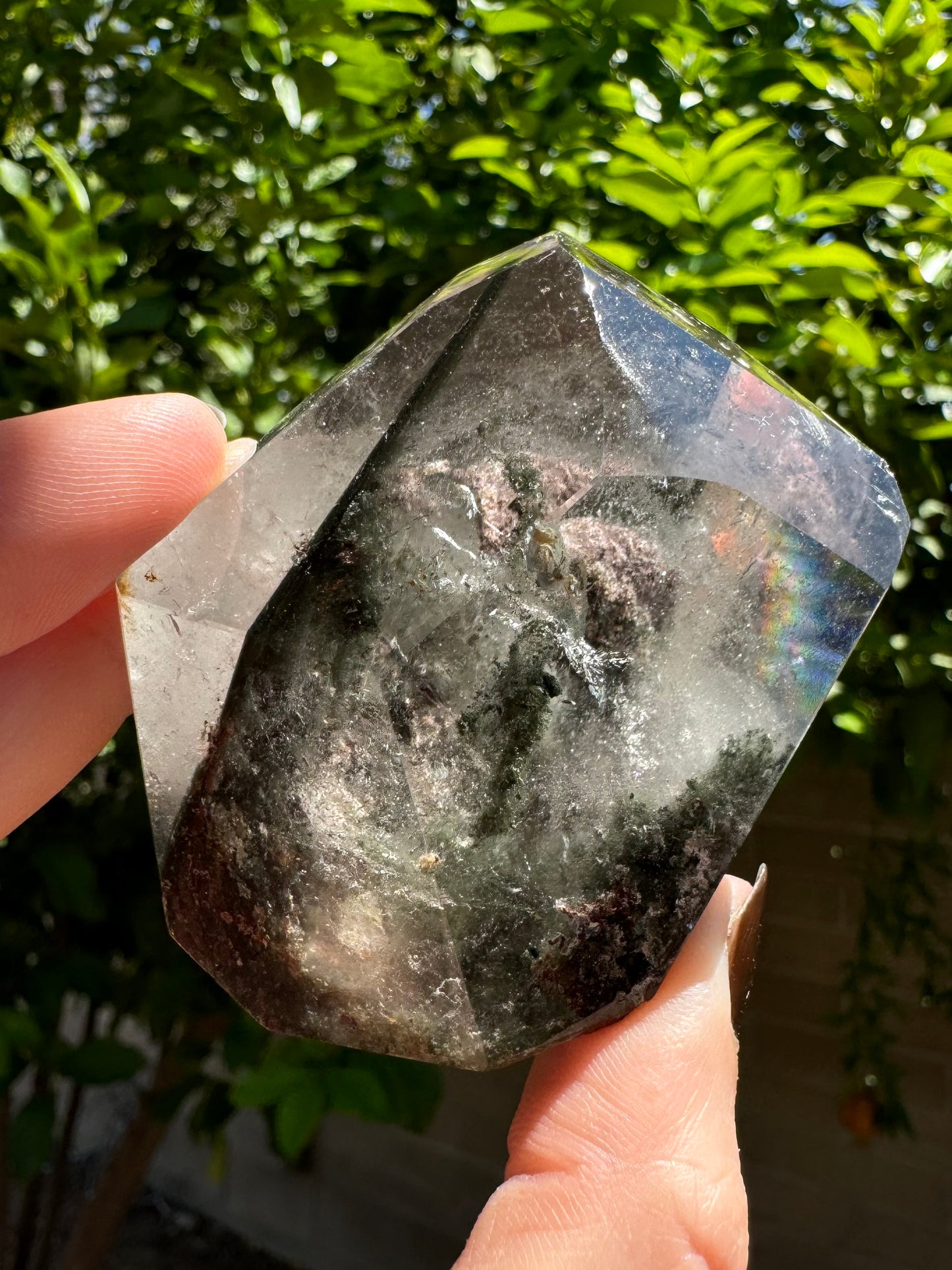 The piece angled so the spherical pink inclusion is doubled, visible in double-view through two faces. The clear quartz reflects a rainbow in the upper right.