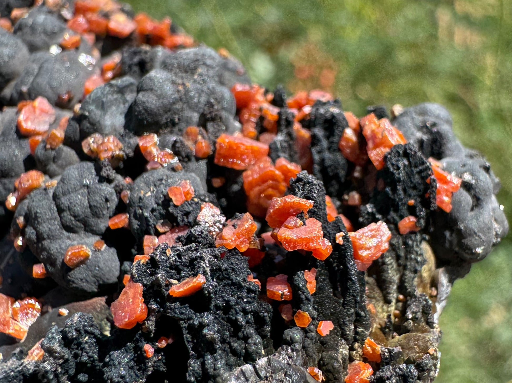 Detail view of hexagonal vanadinite crystals on the edge of the specimen, covering craggy black spires with botryoidal growth behind. The crystals have complex details, with intergrown stepped crystals and geometric edges.