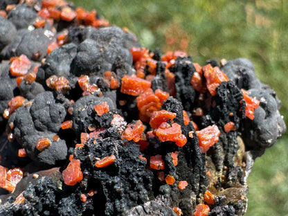 Detail view of hexagonal vanadinite crystals on the edge of the specimen, covering craggy black spires with botryoidal growth behind. The crystals have complex details, with intergrown stepped crystals and geometric edges.