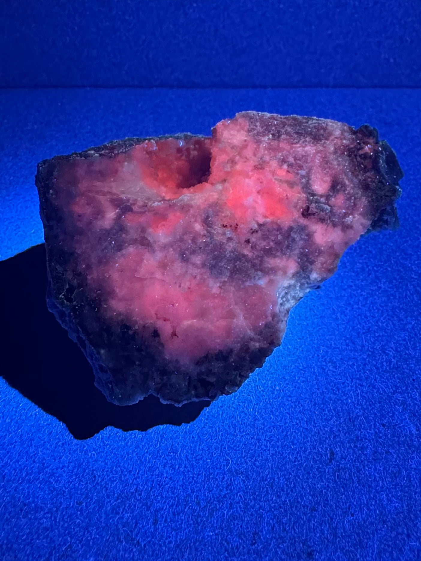 The specimen illuminated in UV light, with patchy peach-red glow. The pocket fluoresces well.