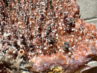 Detail of an edge of the piece with white spheres and lumpy brown mineral on spires. In the foreground some spires are broken, revealing rings of orange, white, and a dark mineral or hollow.