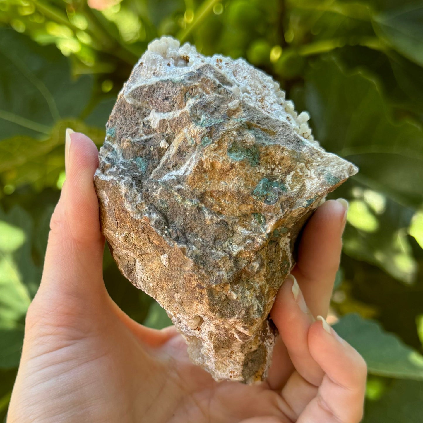 The back of the piece, a light brown rough rock matrix with patches of a green mineral in it and veins of white mineral.