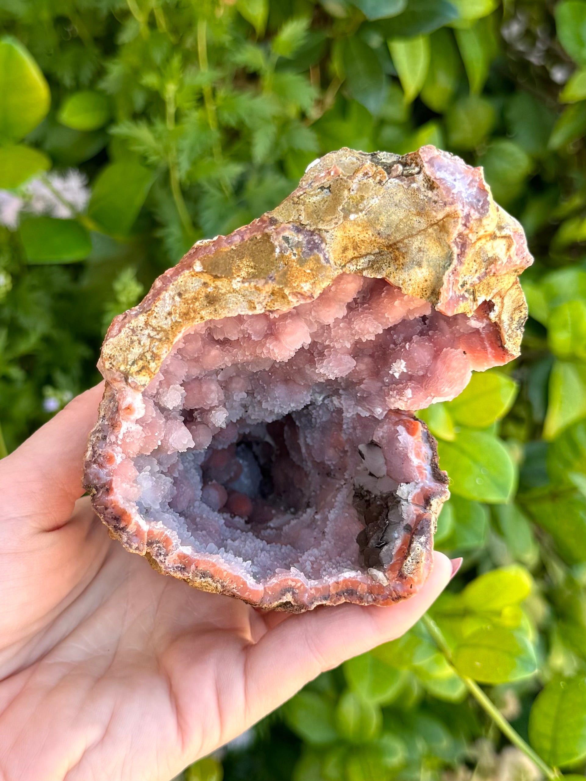 Looking down into the geode at an angle, highlighting the surface pattern of bands of larger quartz crystals crossing one side and large botryoidal forms on the other. A cluster of dark brown mineral is visible at the rim.