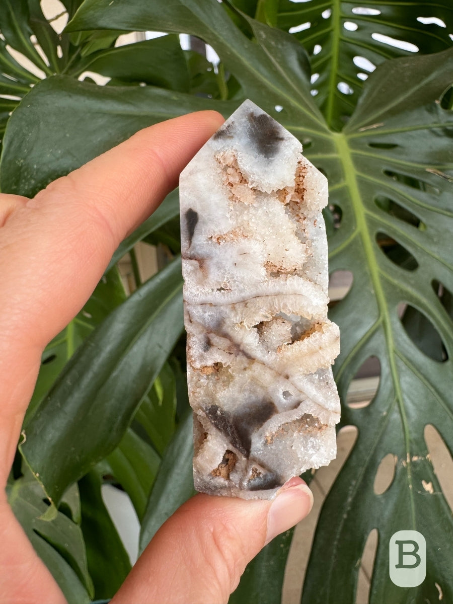 Option B, a short wide four-sided tower carved of opaque, matte white chalcedony, with dark brown-gray veining, and cavities lined with druzy.