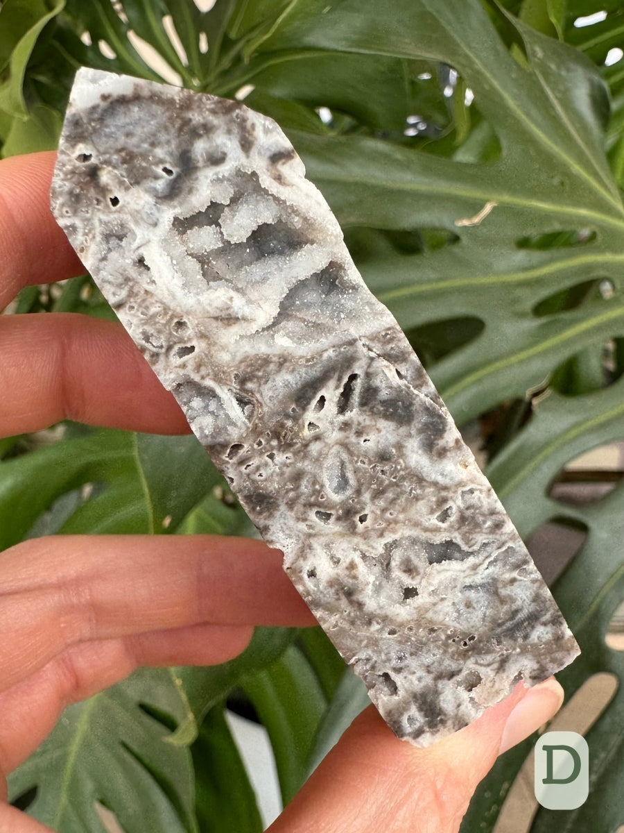 Option D, a four-sided tower of matte, opaque white chalcedony with gray patterning. There is a large cavity near the top, with lumpy forms through it and lined with quartz druzy.