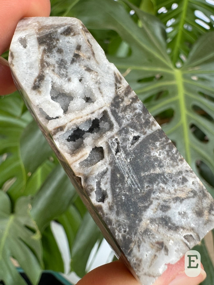 Option E, an opaque matte four-sided tower, white chalcedony with dark patches. There are cavities with veins through them, lined with druzy.